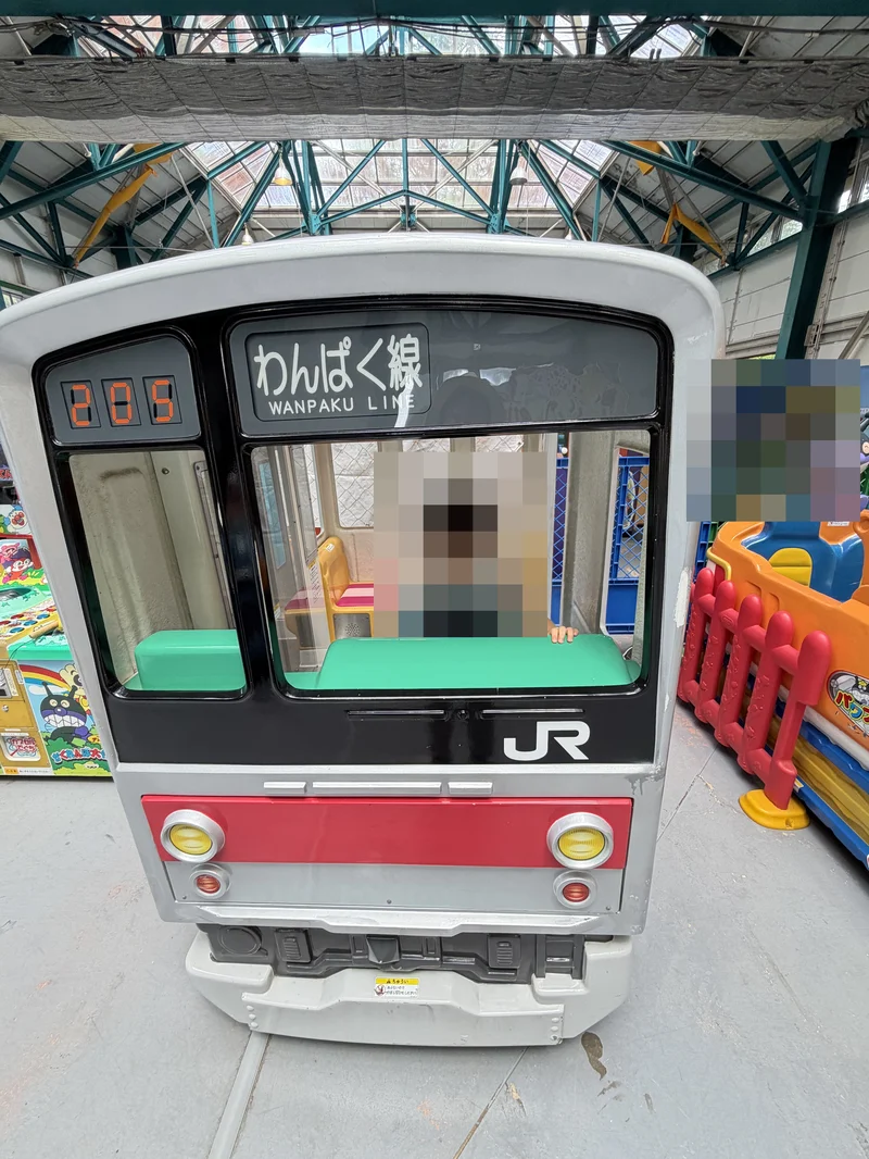 屋根のあるエリアに置かれた電車型の遊具に乗る子ども