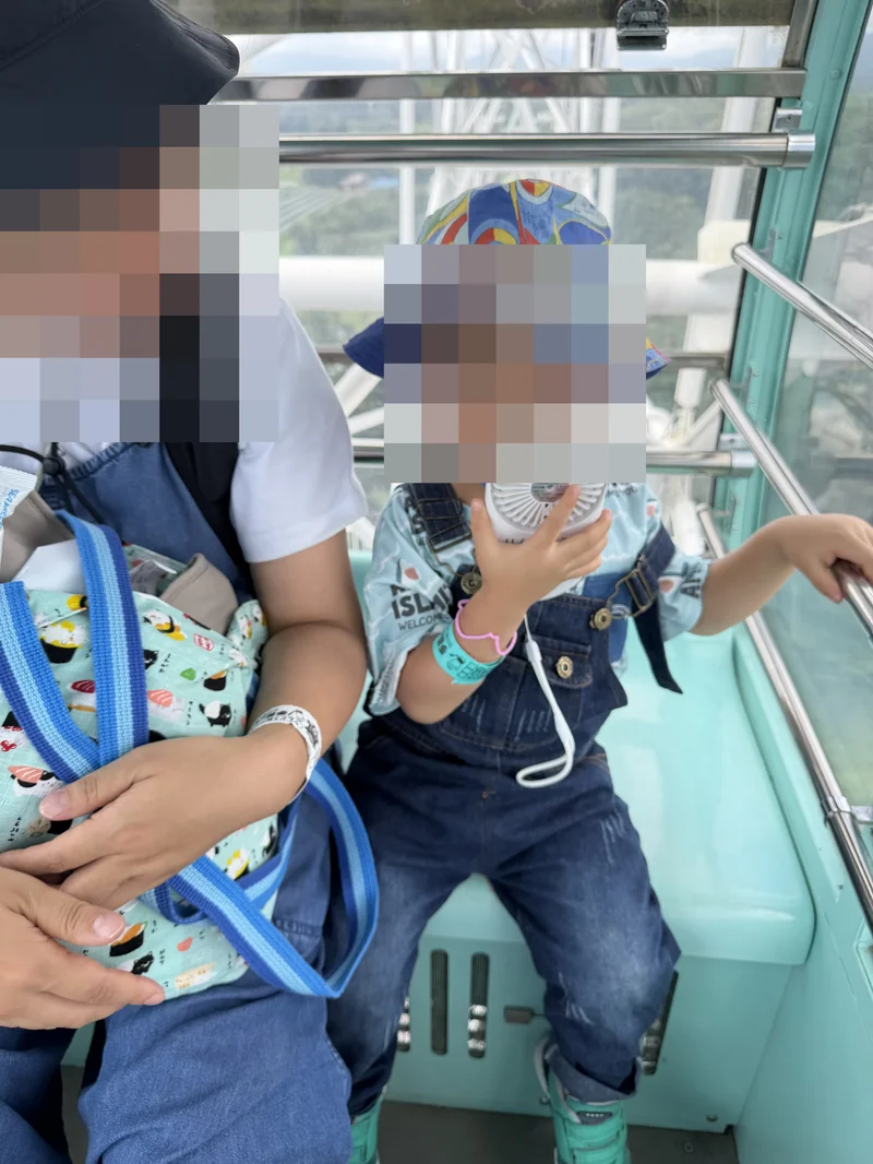 観覧車のゴンドラ内で備え付けの扇風機を顔に当てる3歳児
