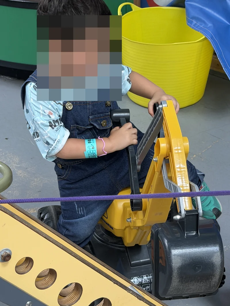 黄色い重機の遊具のレバーを両手で操作する3歳児